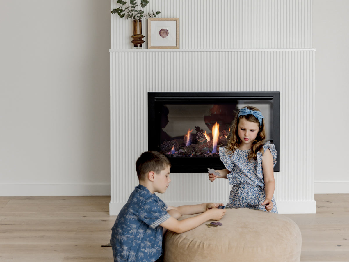 Two children in front of an escea fireplace with a white mantel.